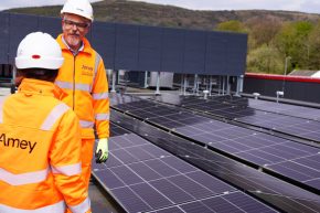 Two Amey employees in PPE in conversation. To their right is solar panels.