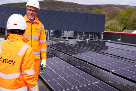 Two Amey employees in PPE in conversation. To their right is solar panels.